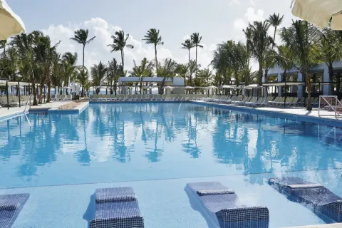 Wide pool with in-water loungers, palms, and shaded seating at Hotel Riu Bambu.