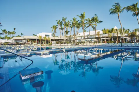 Pool with submerged stools, tables, loungers, and palm-lined buildings at Hotel Riu Bambu.