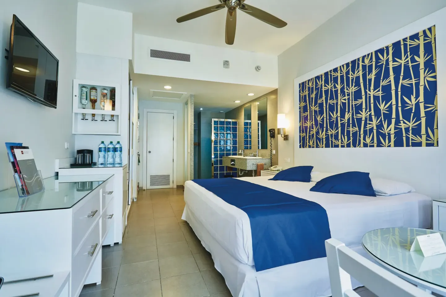 Deluxe Room with bed, wall-mounted TV, drinks area, and open bath at Hotel Riu Bambu.