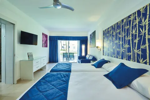 Family Room with two beds, blue sofa, TV, and balcony at Hotel Riu Bambu.