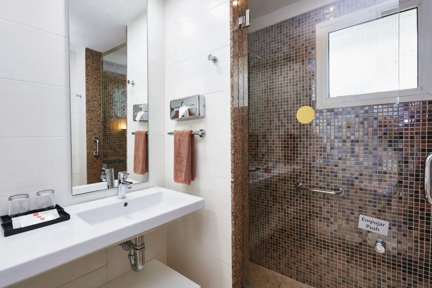 Guest room bathroom with a sink, mirror and glass shower with mosaic tile at Hotel Riu Bambu.
