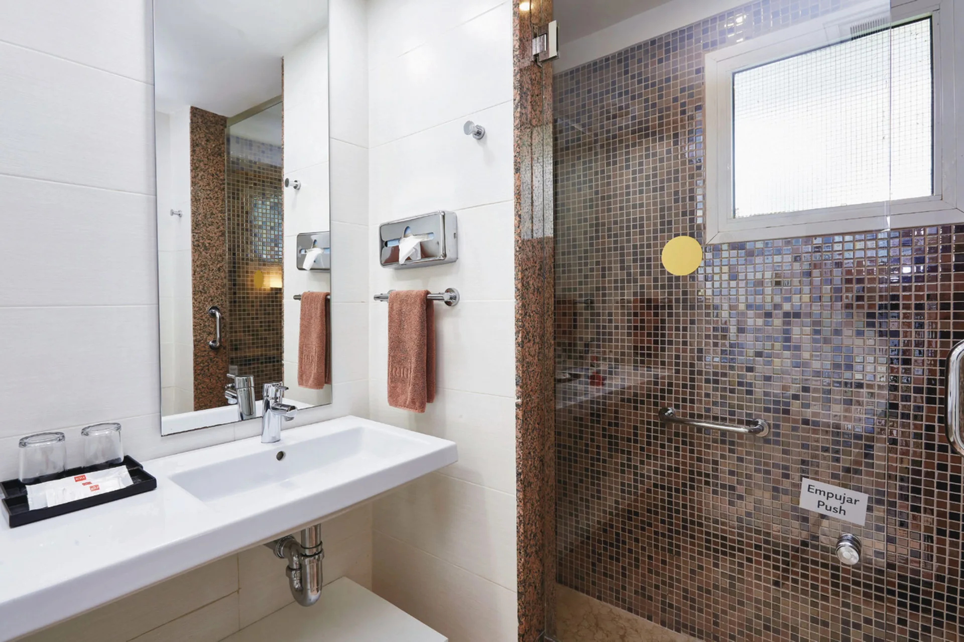 Guest room bathroom with a sink, mirror and glass shower with mosaic tile at Hotel Riu Bambu.