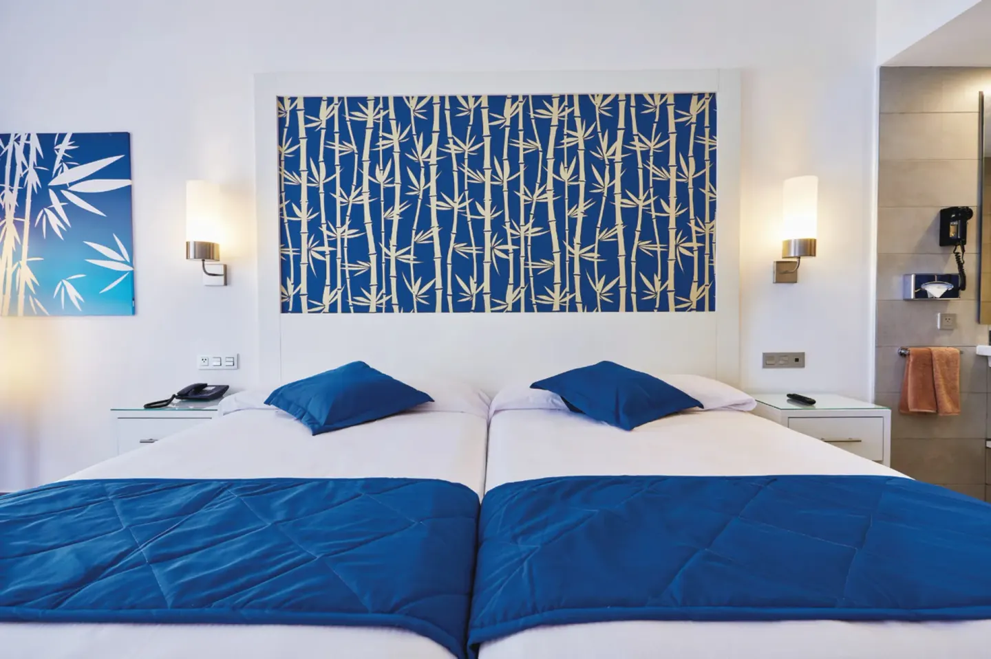 Guest room with two double beds, blue bedding and an open bathroom view at Hotel Riu Bambu.