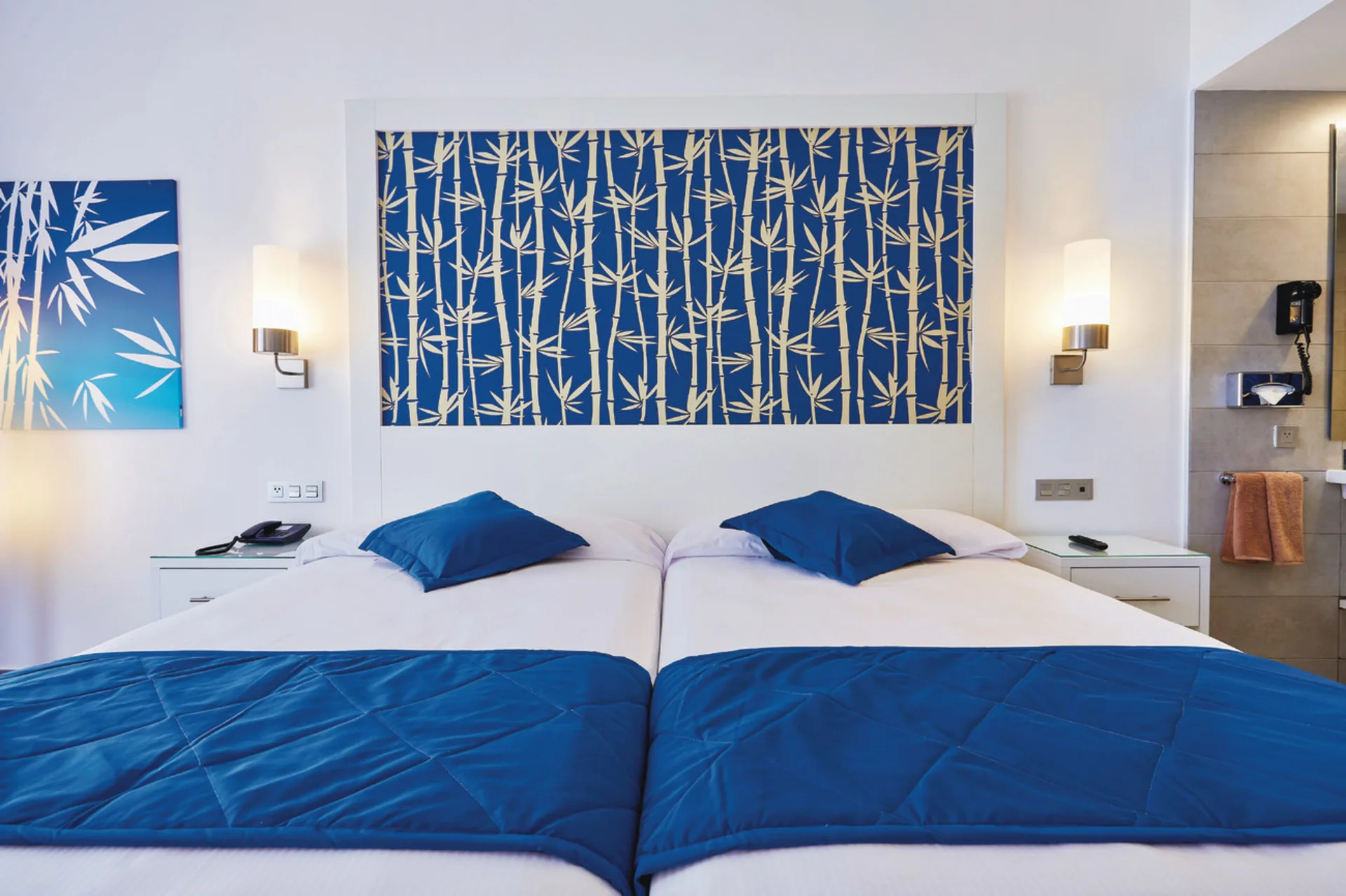 Guest room with two double beds, blue bedding and an open bathroom view at Hotel Riu Bambu.