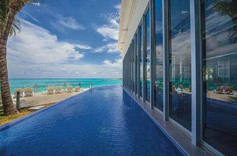 Infinity-edge pool at Hotel Riu Cancun beside glass walls and the turquoise sea.