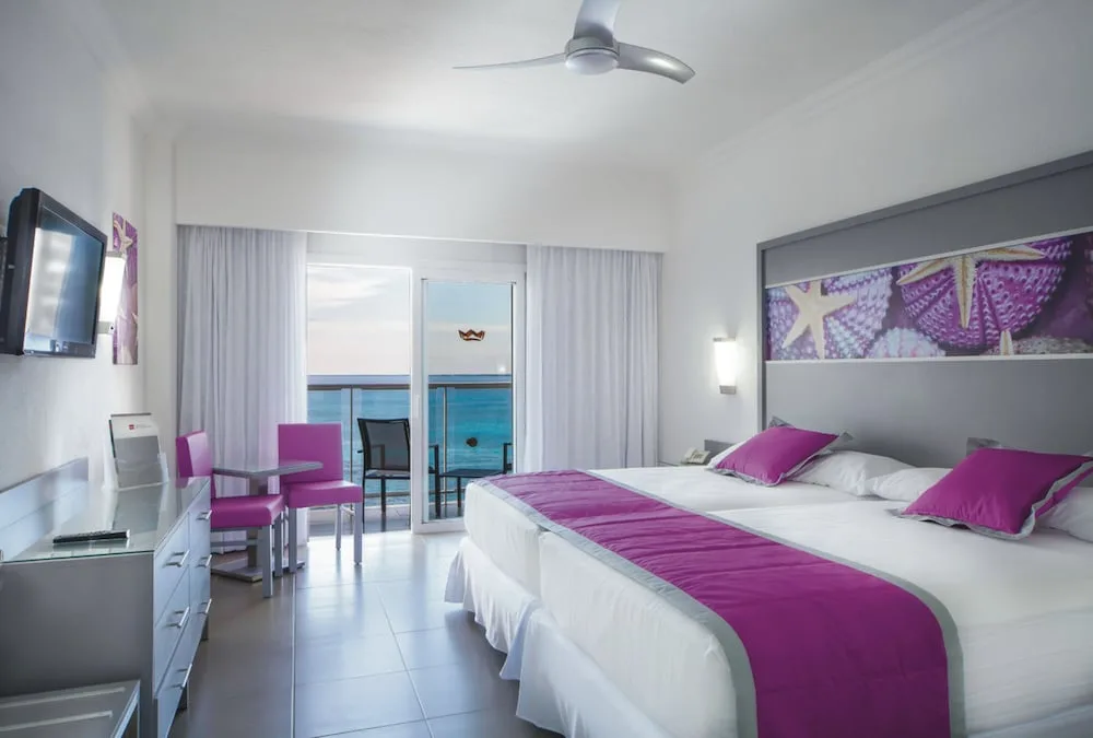 Ocean-view guest room with two beds, desk, and balcony at Hotel Riu Cancun.