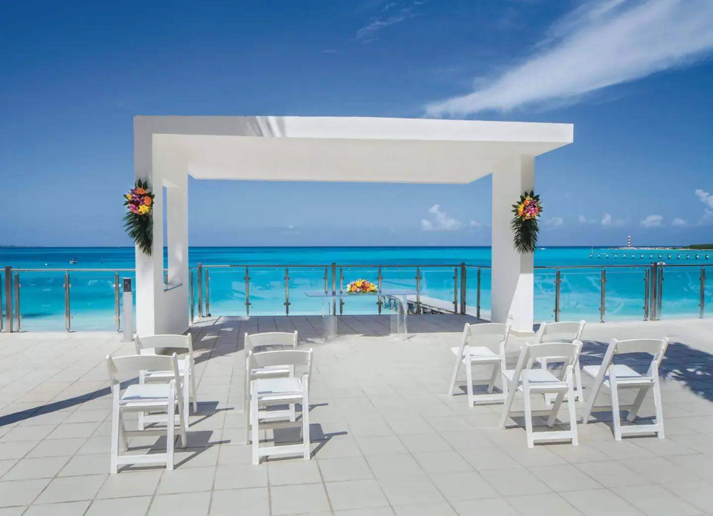 Oceanfront wedding arch with white chairs and flowers at Hotel Riu Cancun.