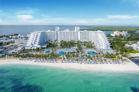 Aerial beachfront view of Hotel Riu Caribe with pools, palms, sand, and blue-green water.