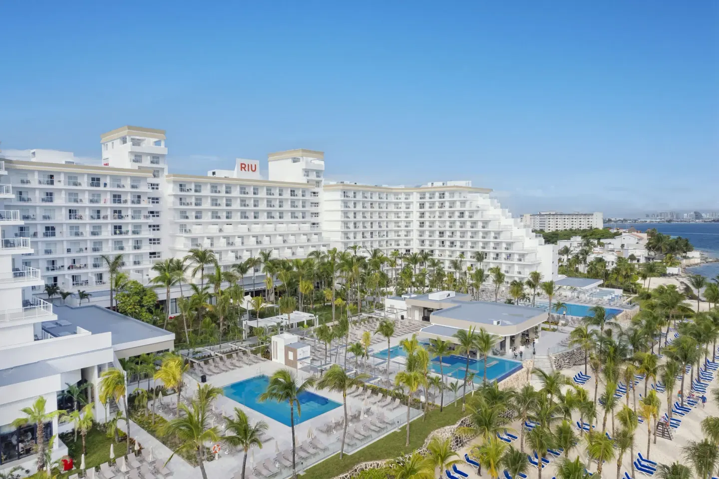 Aerial view of pools, palms, beach loungers, and the white building at Hotel Riu Caribe.