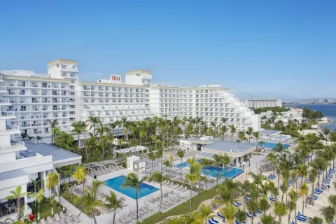 Aerial view of pools, palms, beach loungers, and the white building at Hotel Riu Caribe.