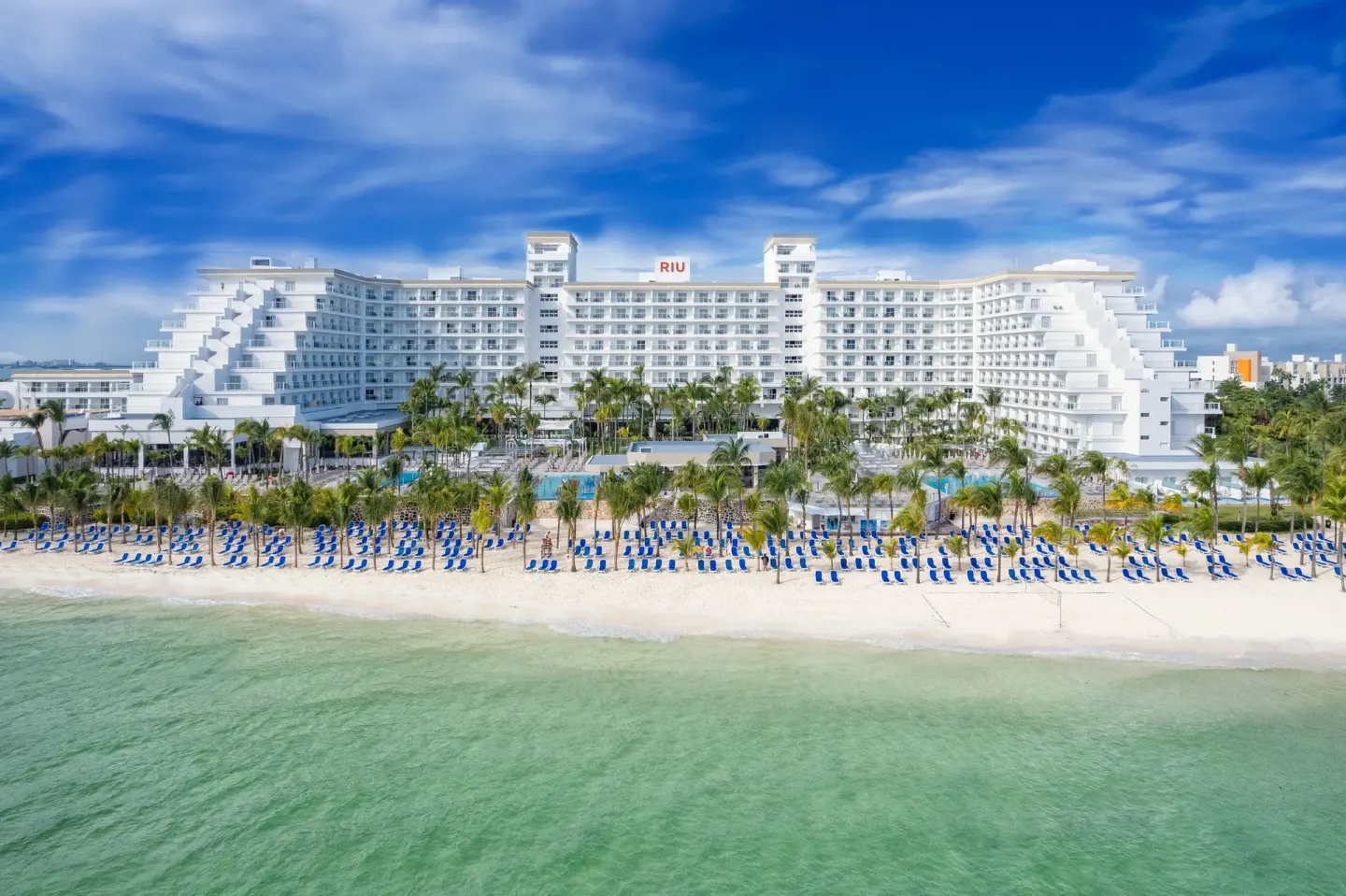 Beachfront exterior, rows of blue loungers, and turquoise water at Hotel Riu Caribe.