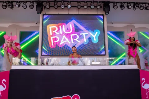 DJ booth and dancers stand before a bright party screen at Hotel Riu Caribe.