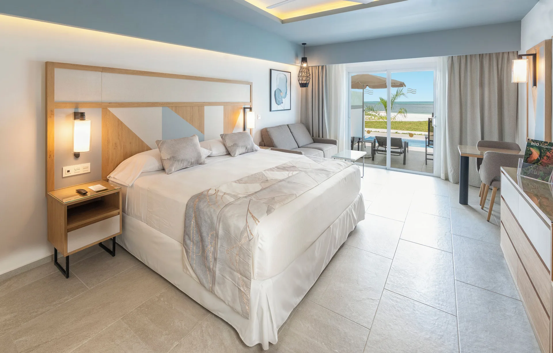 Guest room with a large bed, sofa, desk, and terrace view at Hotel Riu Caribe.
