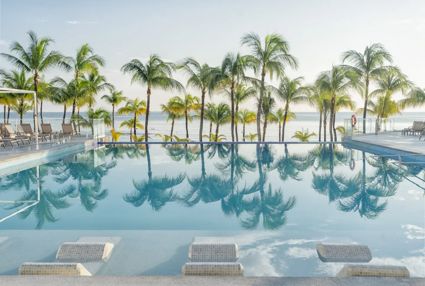 Infinity-style pool reflecting palms with the sea beyond at Hotel Riu Caribe.
