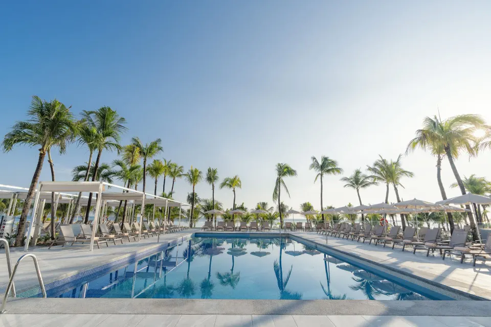 Main pool with loungers, umbrellas, and palm trees at Hotel Riu Caribe.
