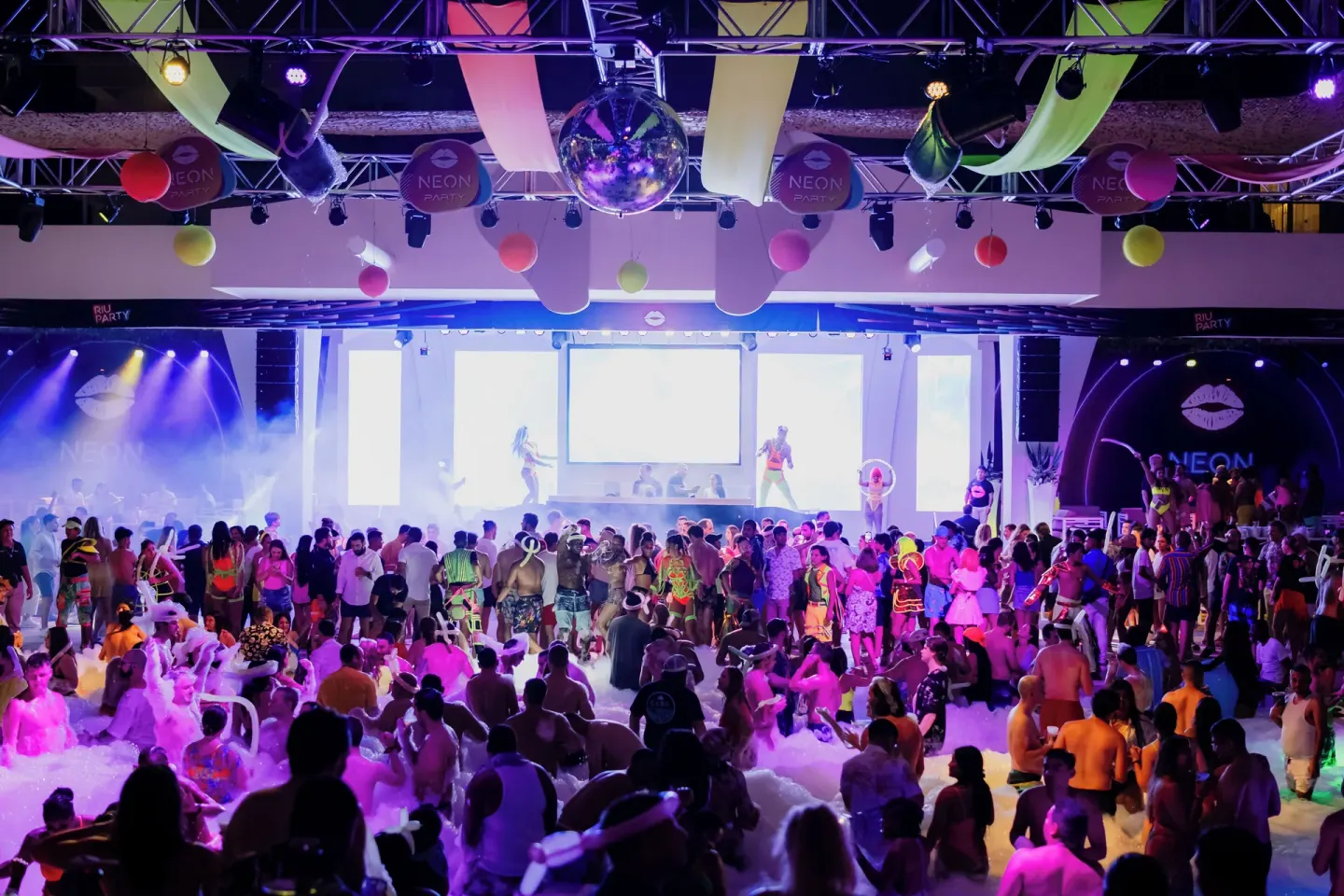 Large neon party crowd fills the dance area at Hotel Riu Caribe.