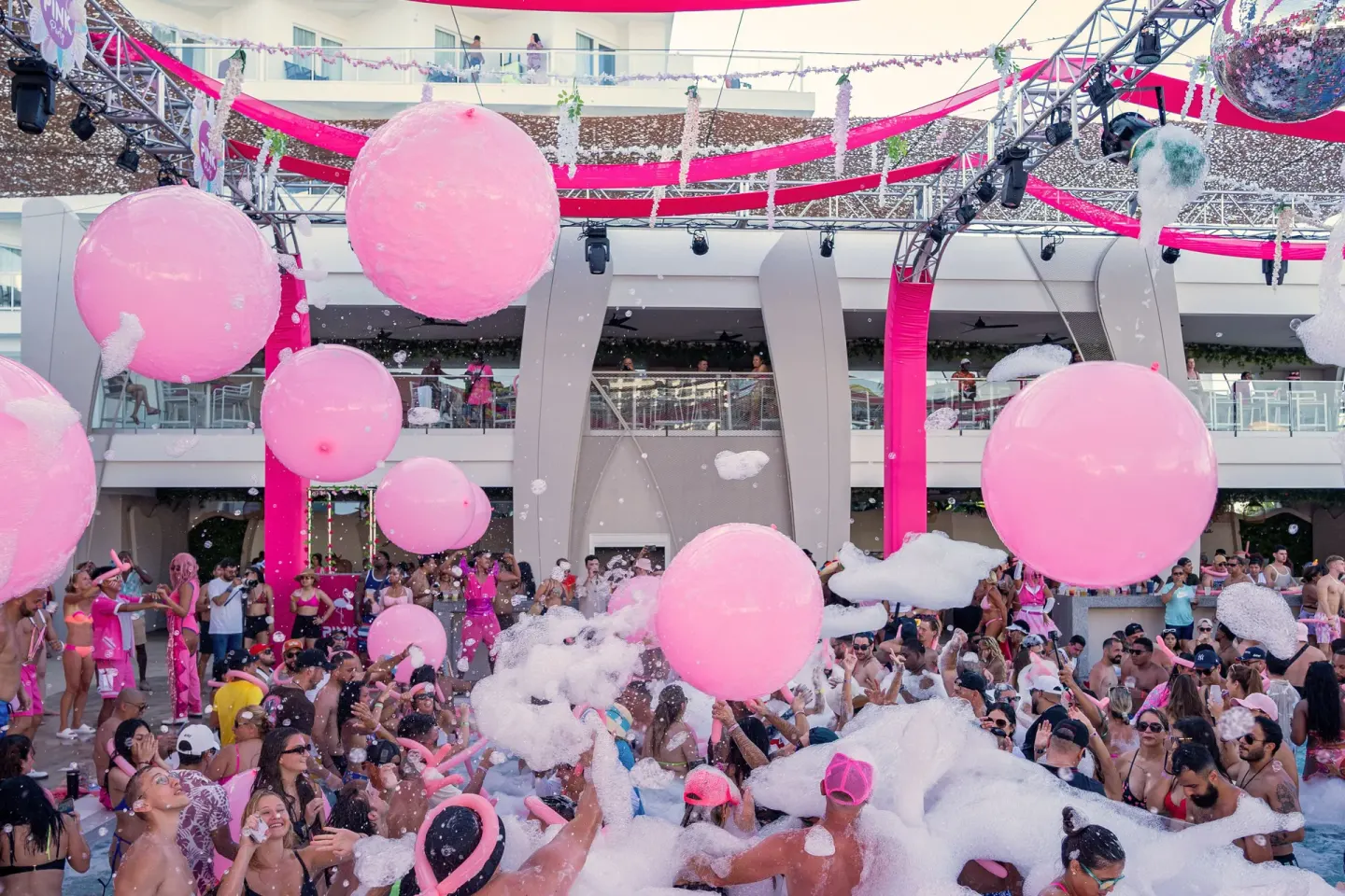 Pool party with foam, pink balloons, and a crowd at Hotel Riu Caribe.