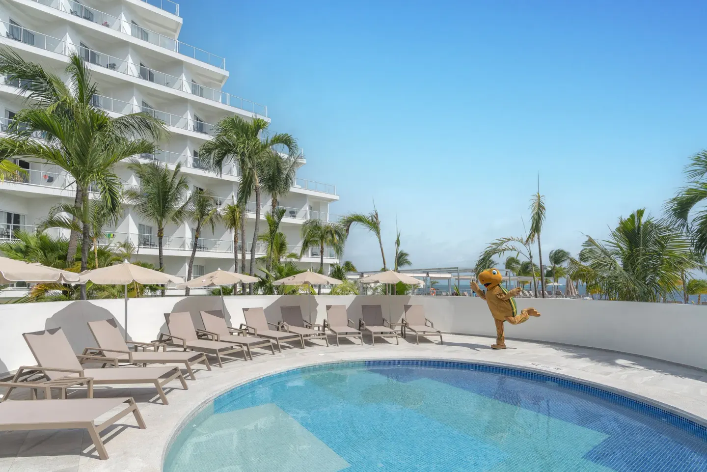 Small pool with loungers, umbrellas, palms, and a mascot at Hotel Riu Caribe.
