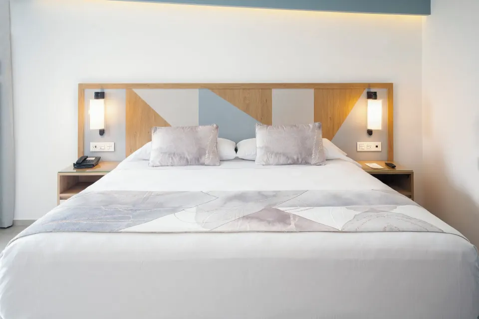 King bed in an Ocean View room at Hotel Riu Caribe with lit wall sconces and a geometric headboard.