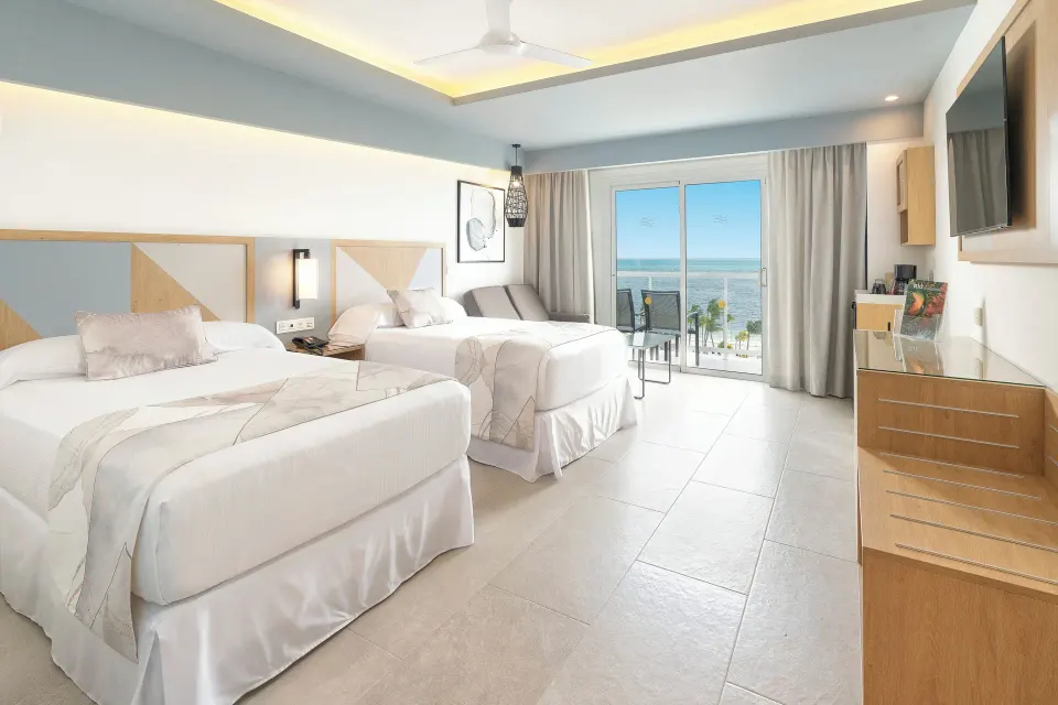 Ocean View room at Hotel Riu Caribe with two beds, balcony seating, and the sea visible through glass doors.