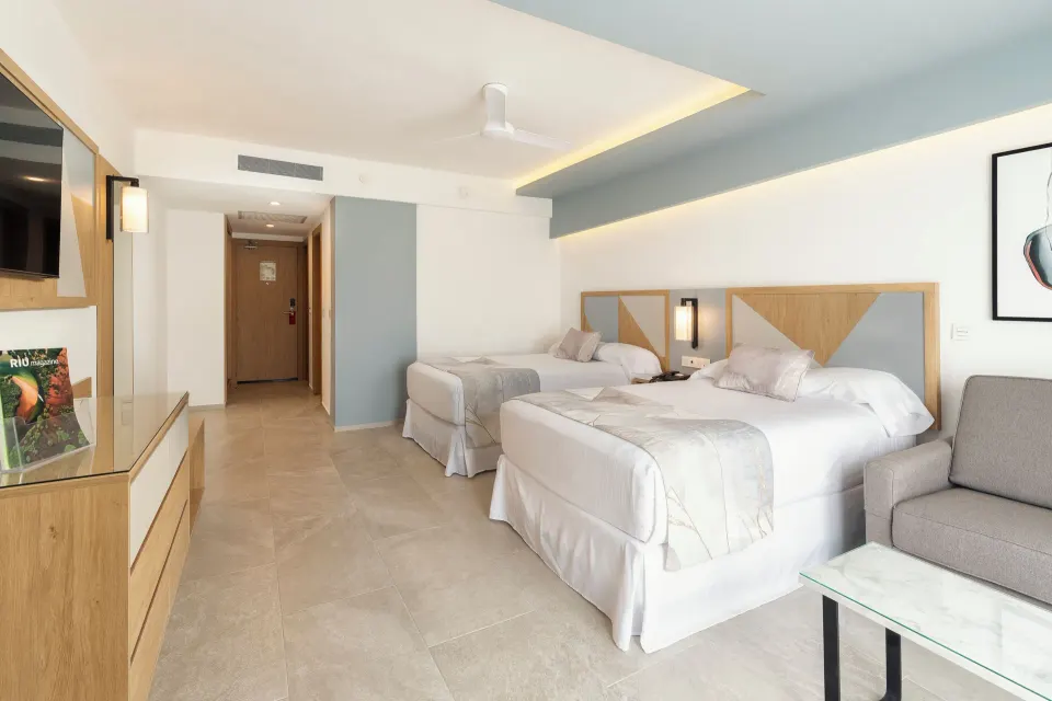 Ocean View room at Hotel Riu Caribe with two beds, sofa, TV console, and entry hall.
