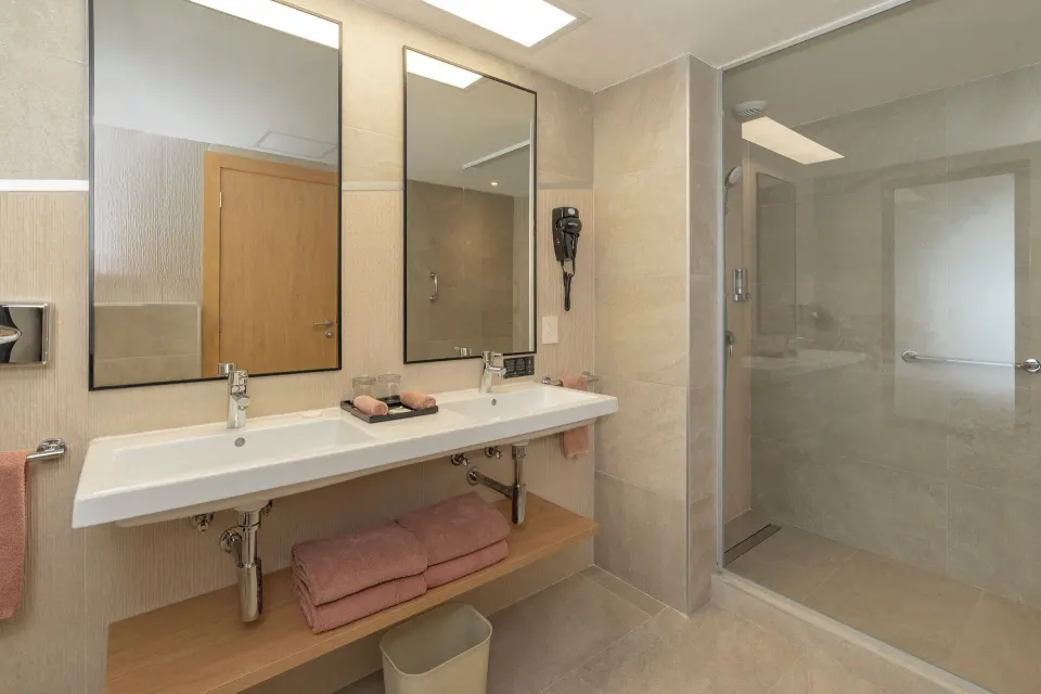Guest room bathroom with double sinks and glass shower at Hotel Riu Caribe.