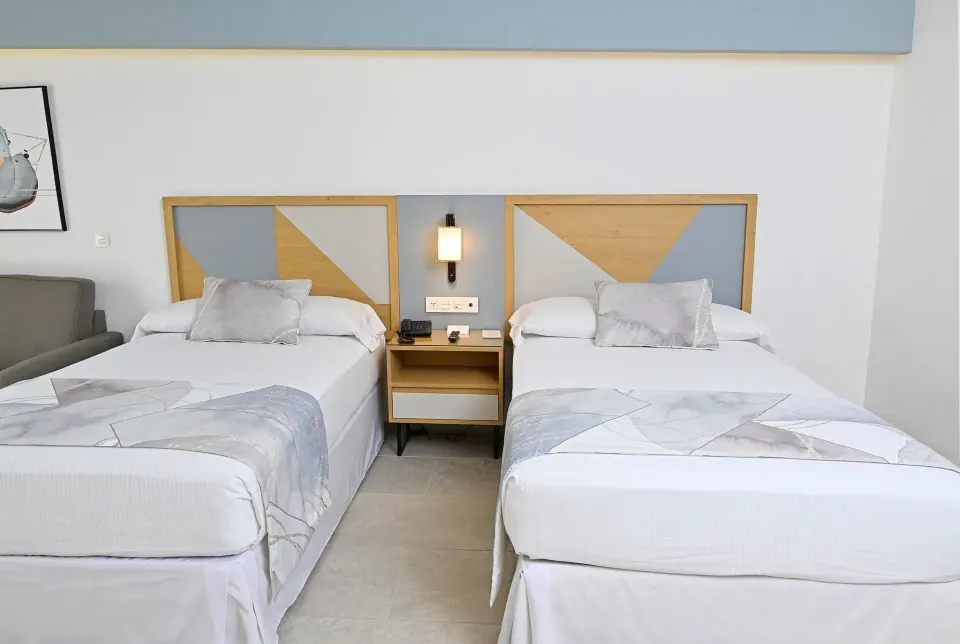 Two double beds with a shared nightstand and wall lamp at Hotel Riu Caribe.