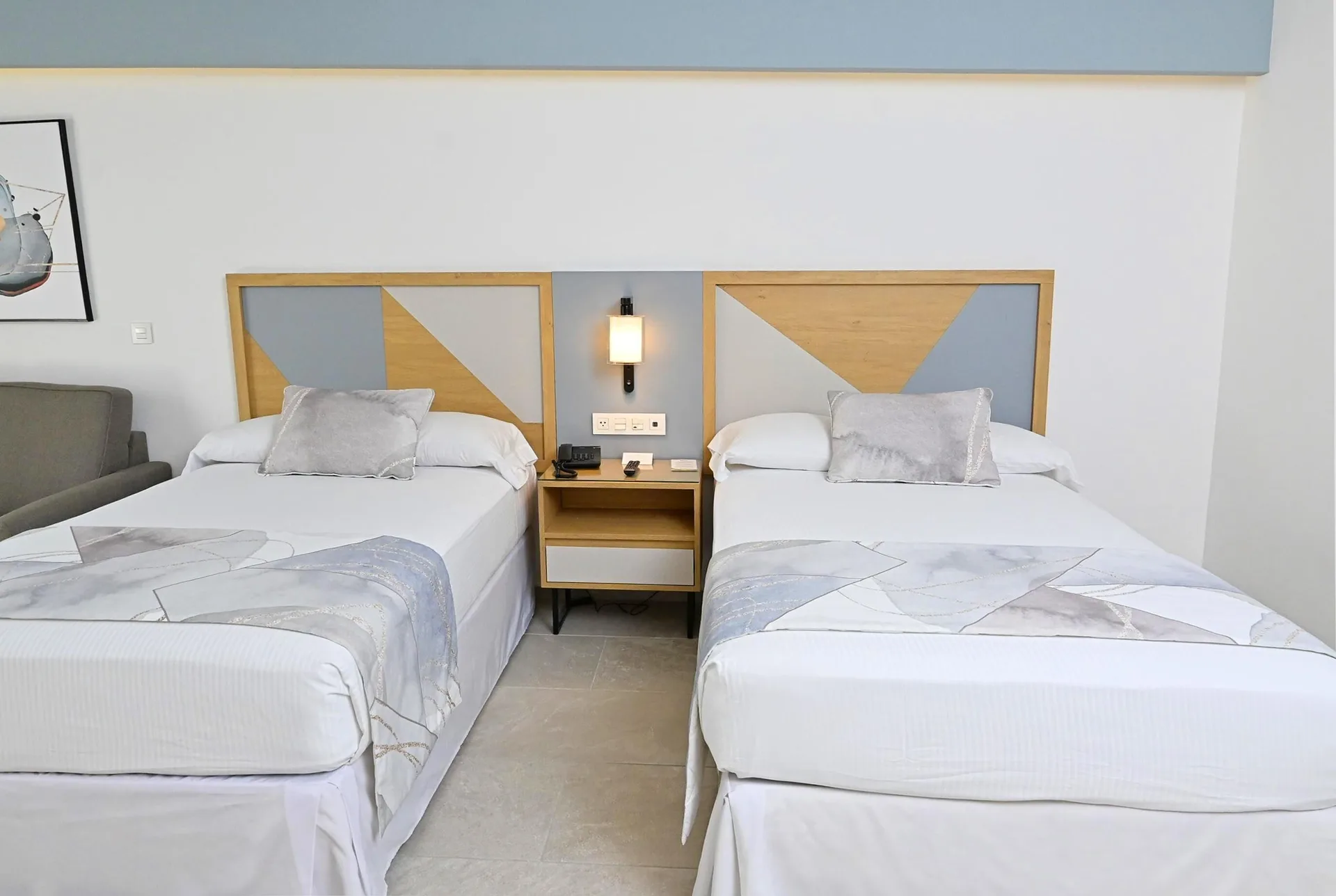 Two double beds with a shared nightstand and wall lamp at Hotel Riu Caribe.