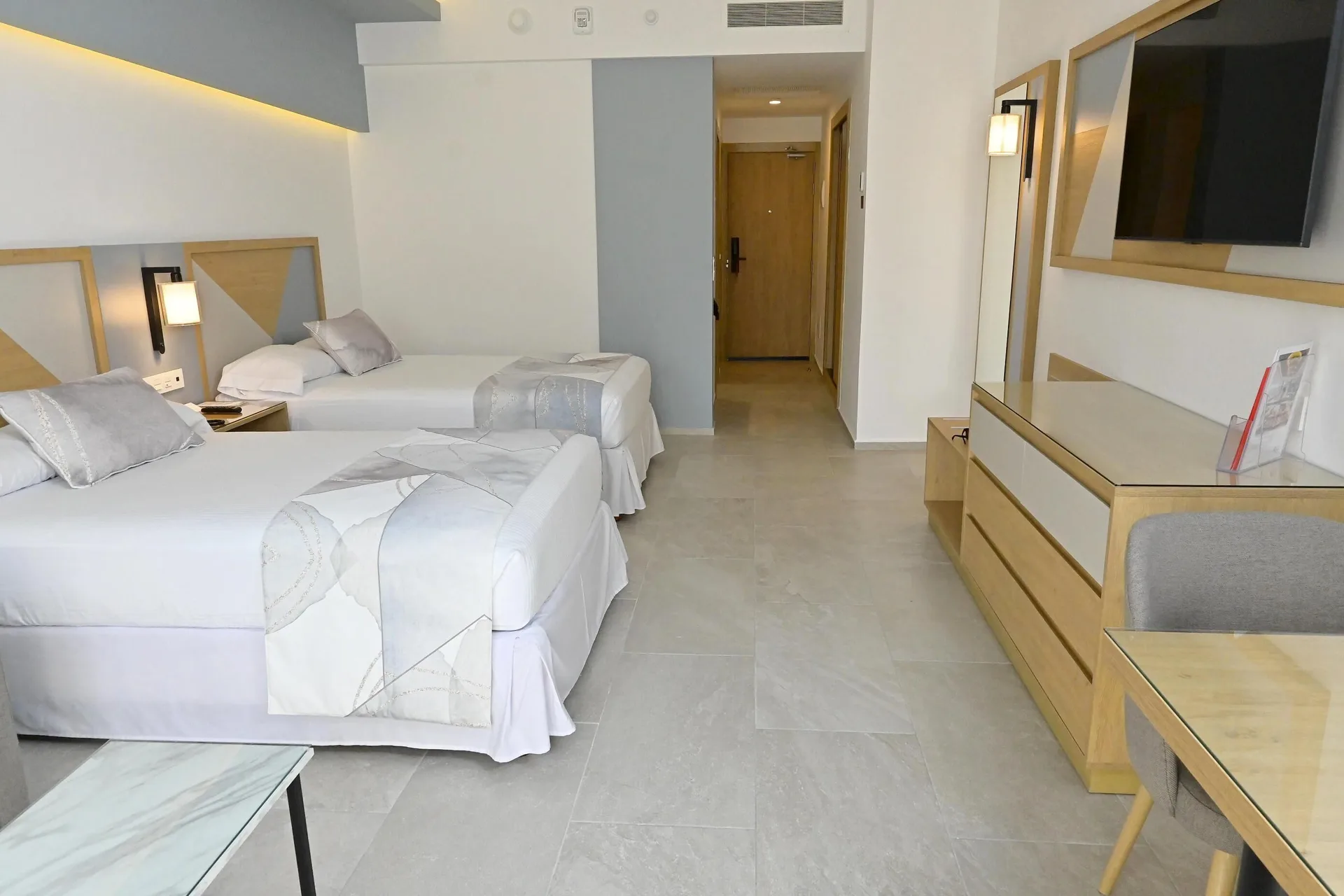 Guest room with two double beds, dresser, desk, and entry corridor at Hotel Riu Caribe.