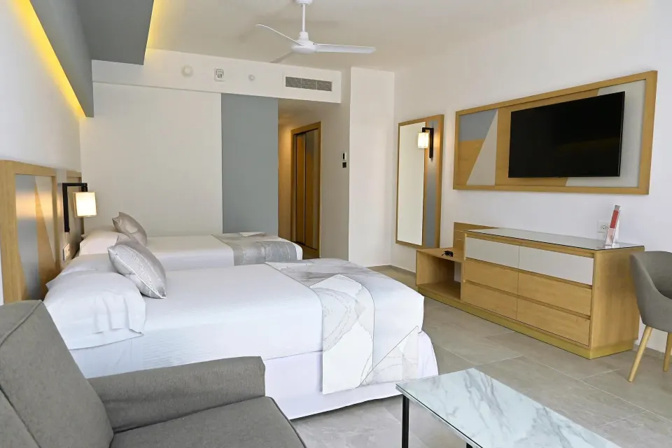 Two double beds with sofa, dresser, mirror, and TV in a room at Hotel Riu Caribe.
