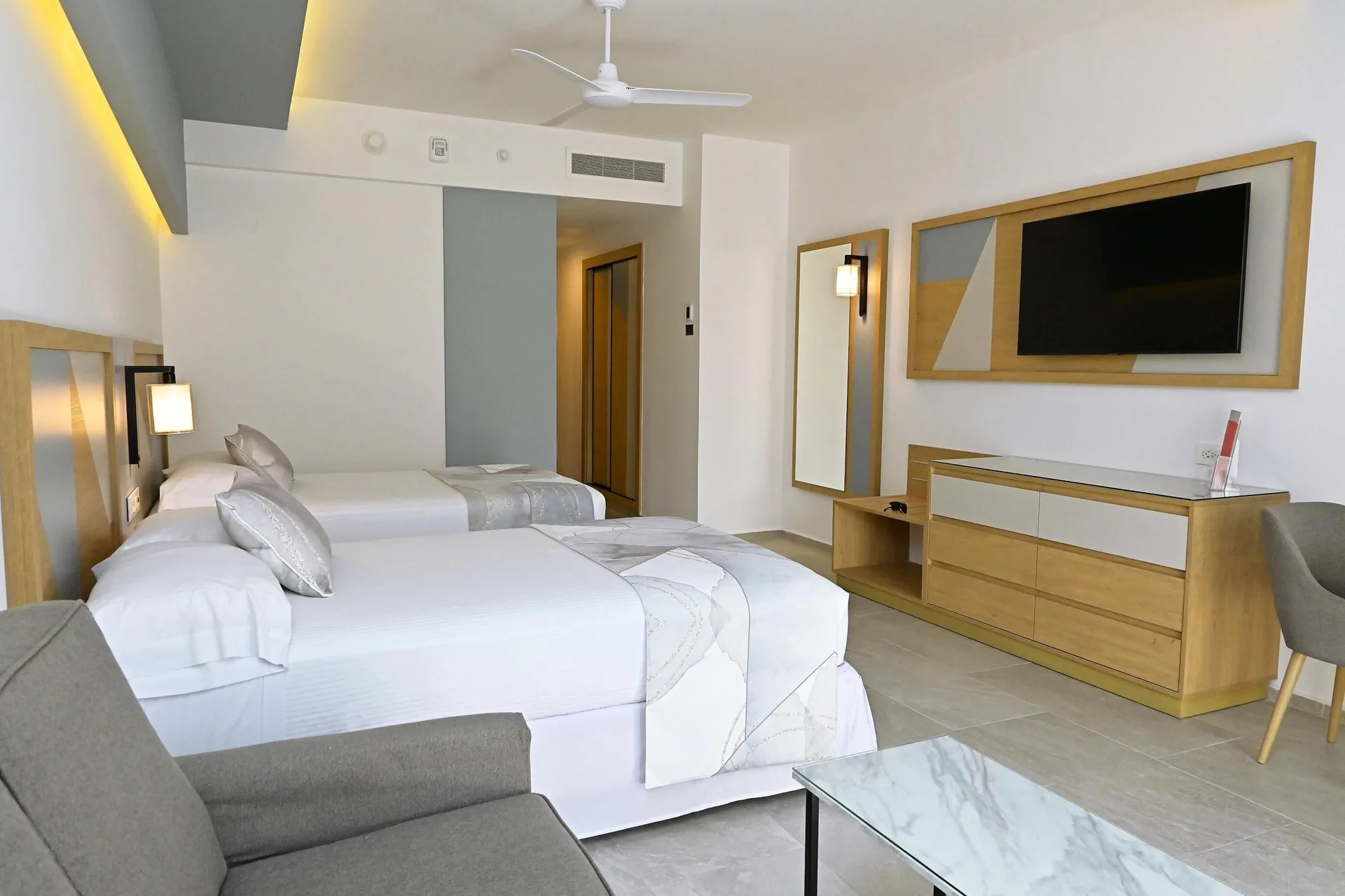 Two double beds with sofa, dresser, mirror, and TV in a room at Hotel Riu Caribe.
