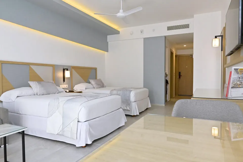 Guest room with two double beds, desk area, and wall-mounted TV at Hotel Riu Caribe.