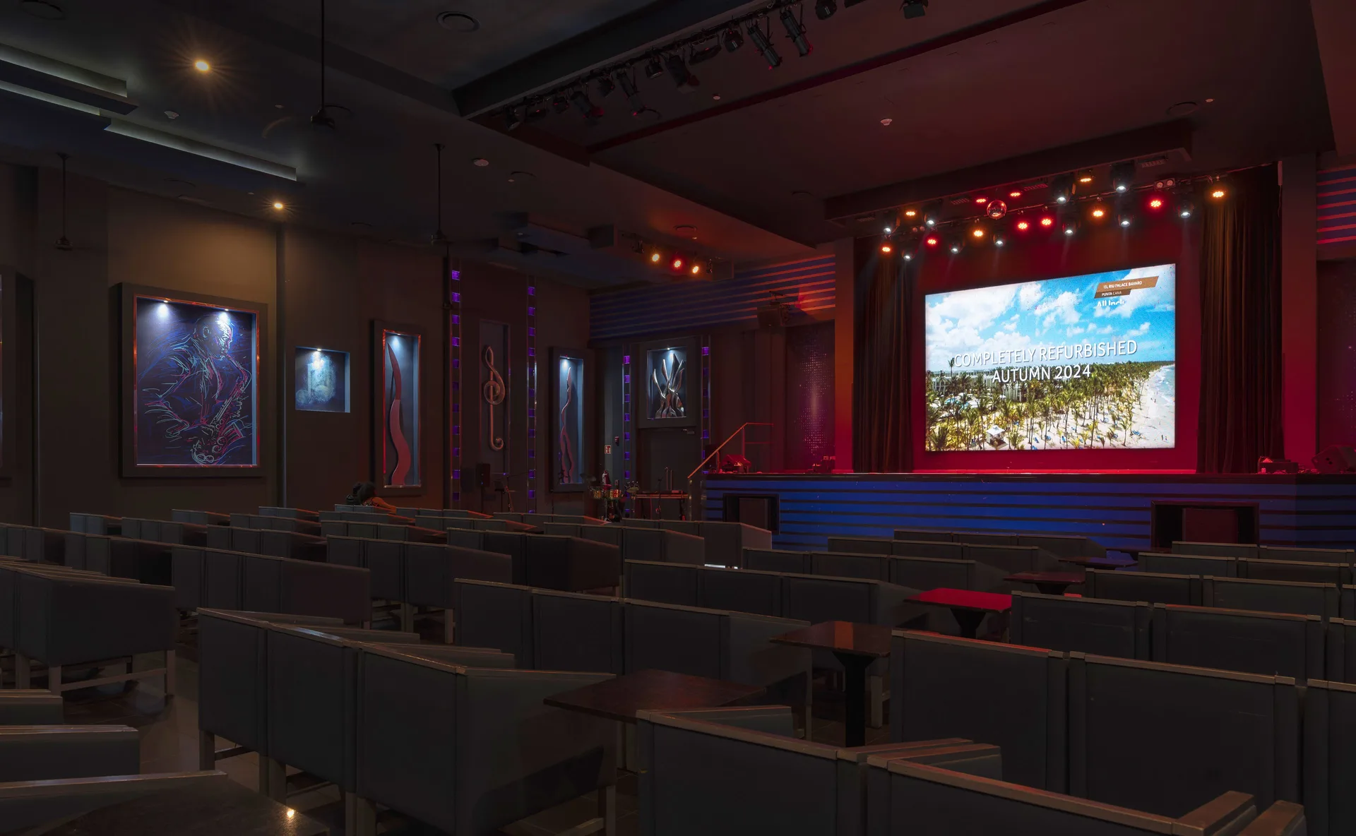 A theater lounge with rows of seats and a lit stage at Hotel Riu Caribe.