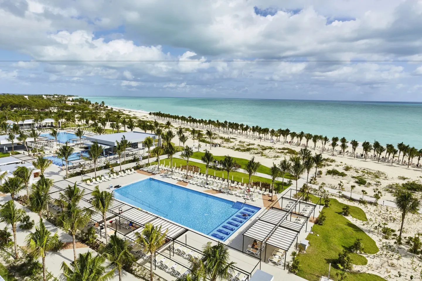An aerial view shows pools, palms, beach, and turquoise sea at Hotel Riu Dunamar.