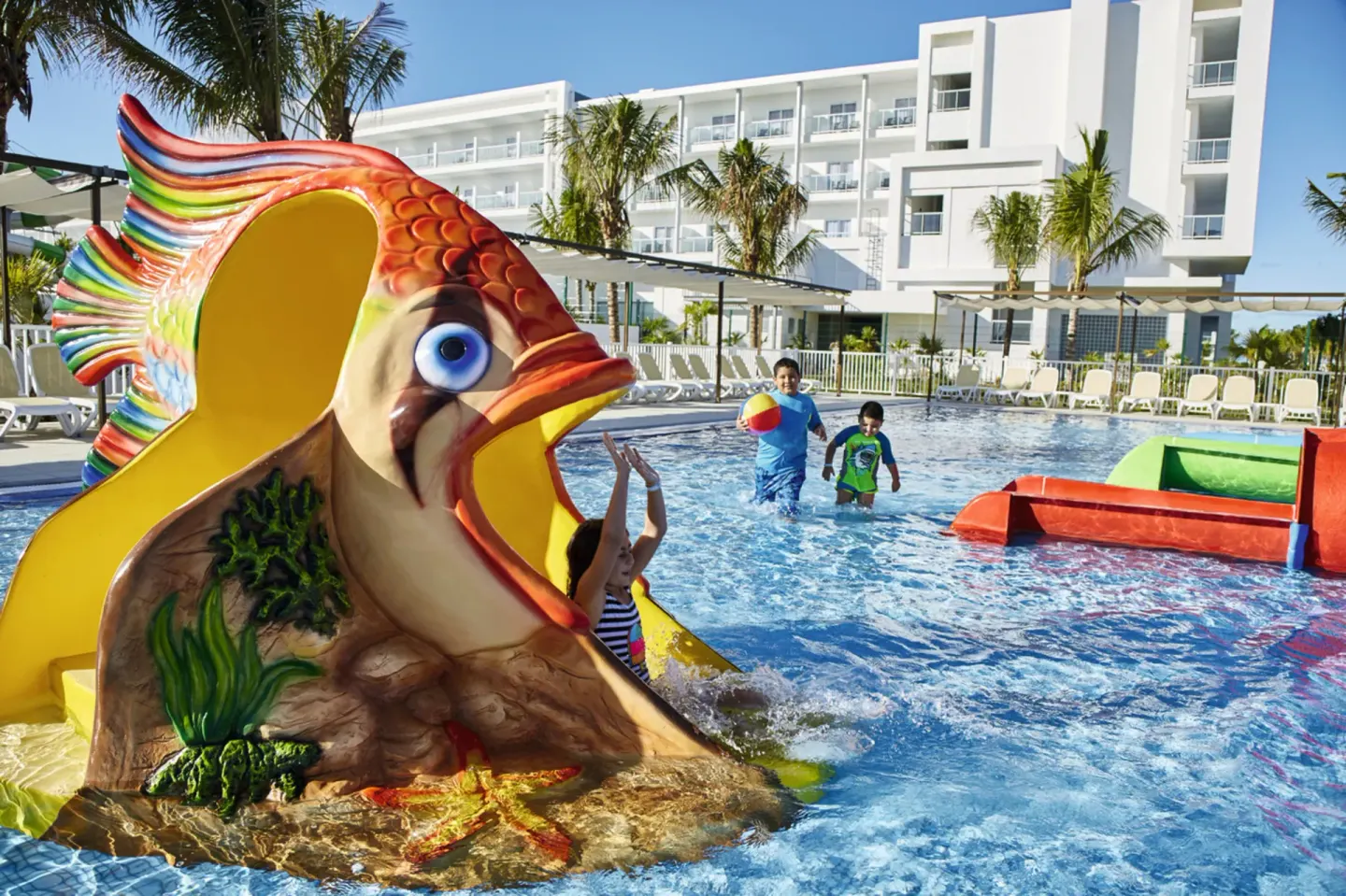 Children play on a colorful fish slide in the pool at Hotel Riu Dunamar.