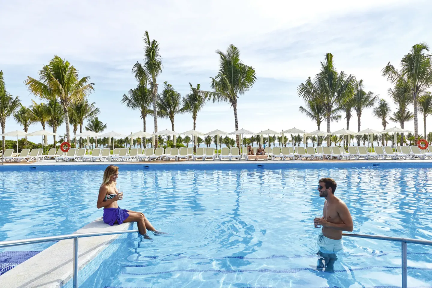 Guests stand and sit at the edge of a large outdoor pool at Hotel Riu Dunamar.