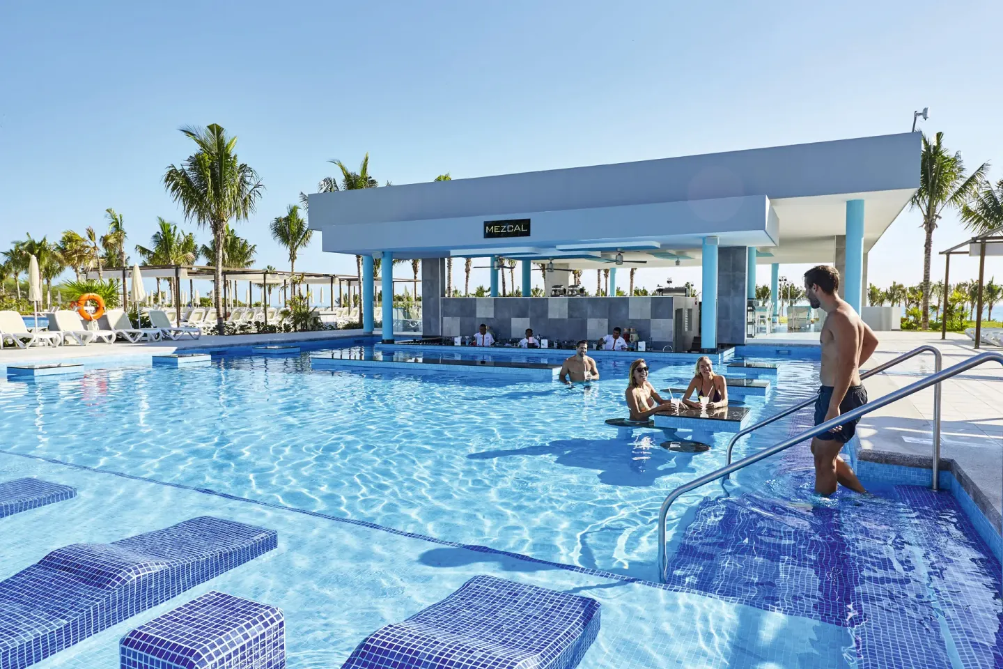 Large pool with swim-up bar and palm trees at Hotel Riu Dunamar.