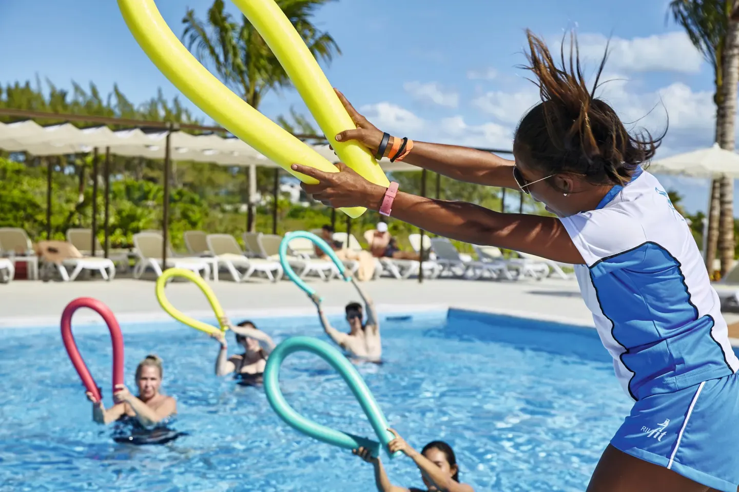 An instructor leads a pool activity with foam noodles at Hotel Riu Dunamar.