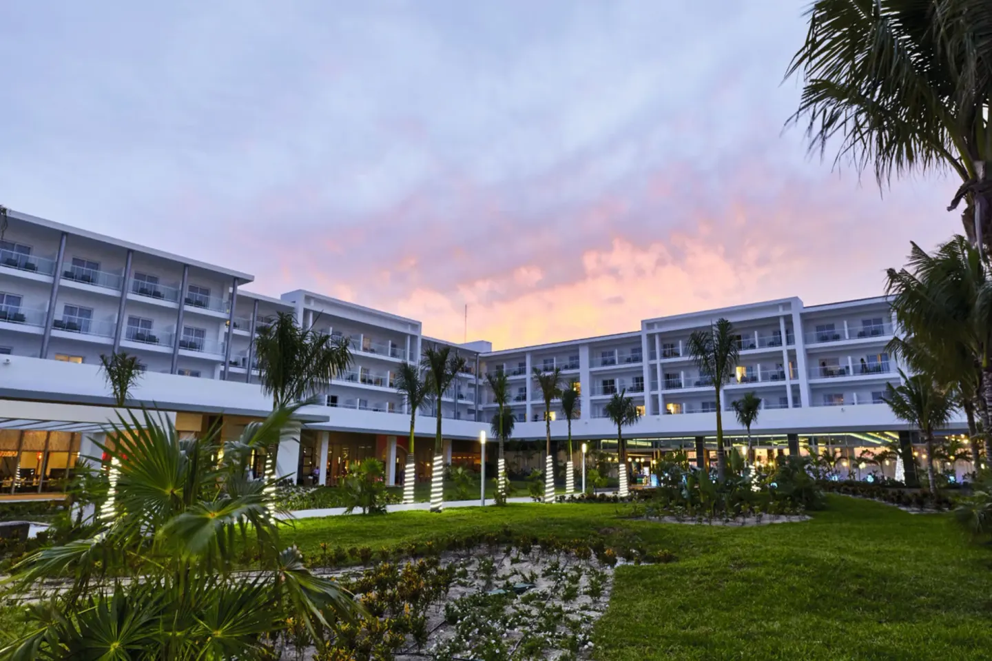 Resort courtyard with palms and guest room balconies at sunset at Hotel Riu Dunamar.