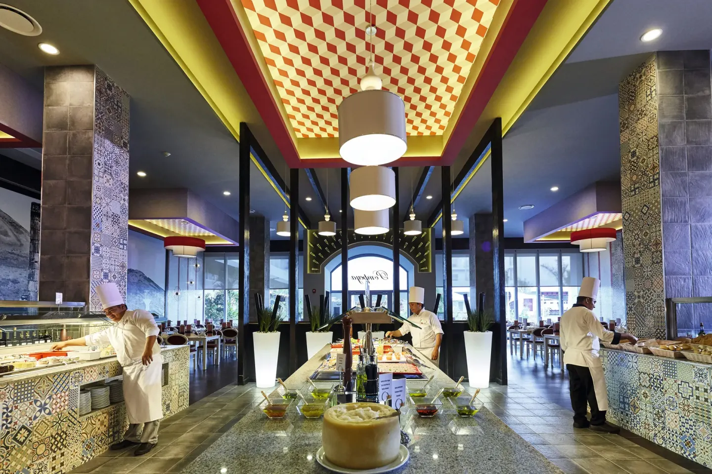 A buffet restaurant with chefs, tiled counters, and central food stations at Hotel Riu Dunamar.