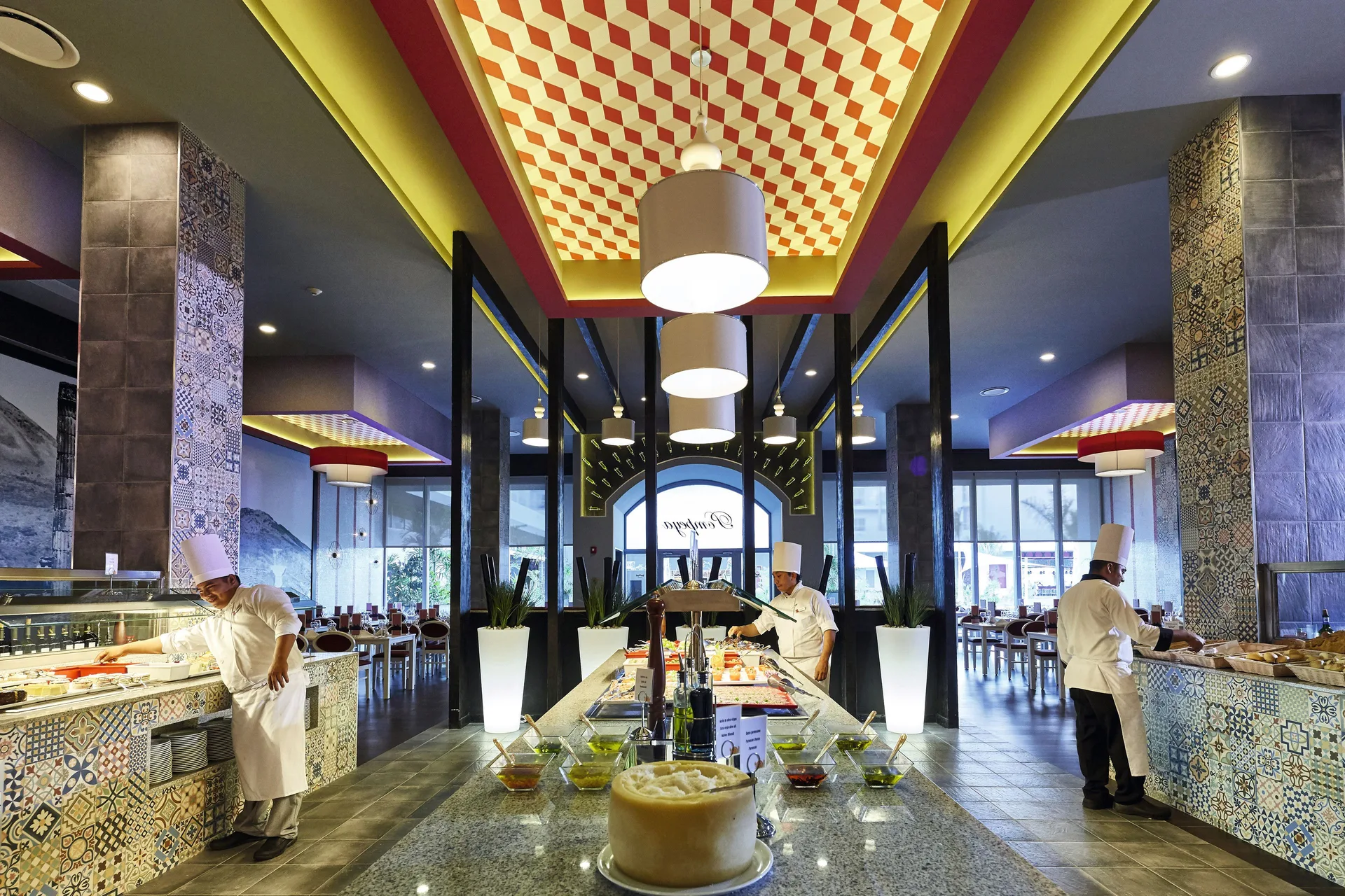 A buffet restaurant with chefs, tiled counters, and central food stations at Hotel Riu Dunamar.