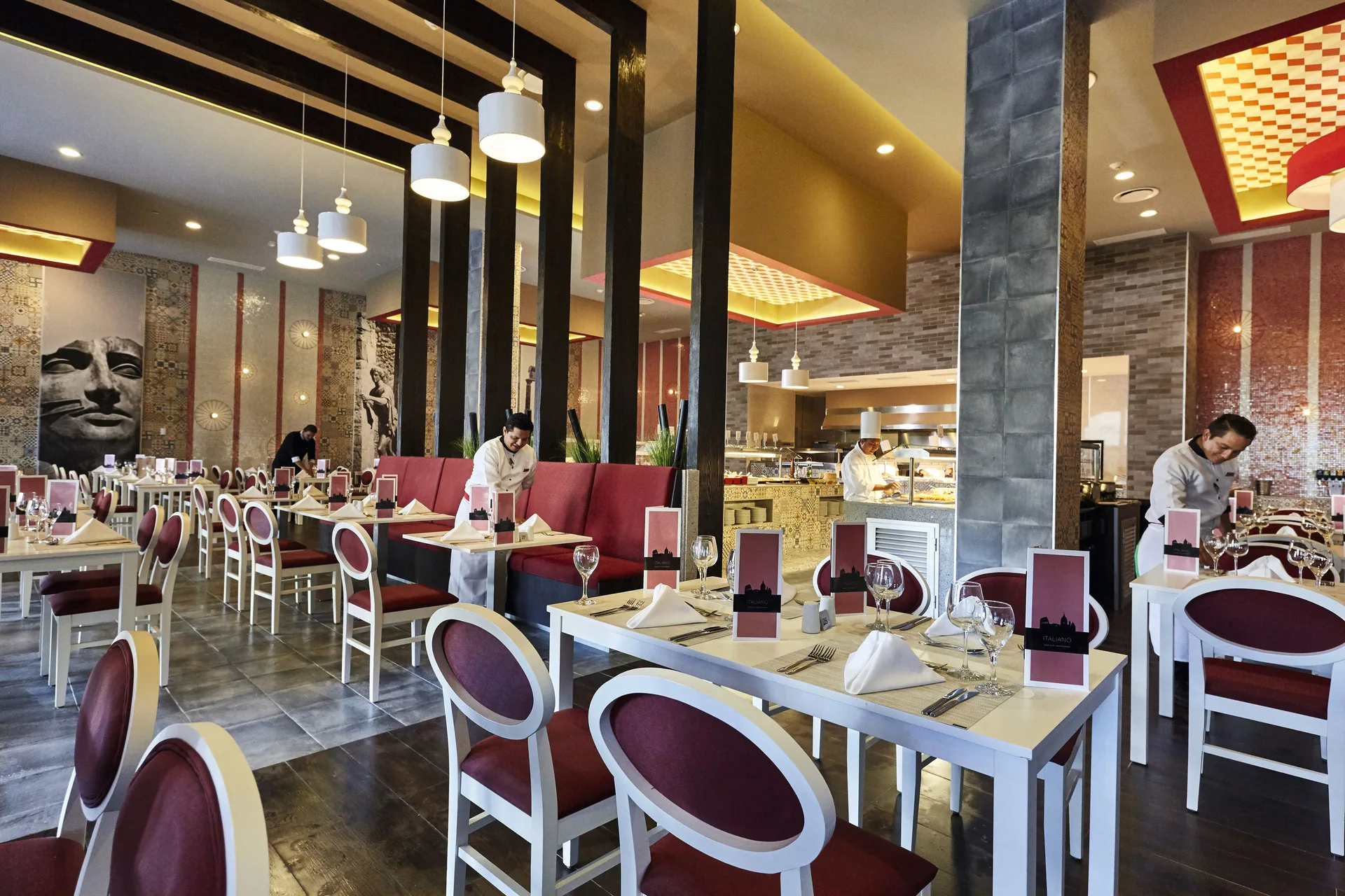An Italian restaurant dining room with red chairs and buffet stations at Hotel Riu Dunamar.