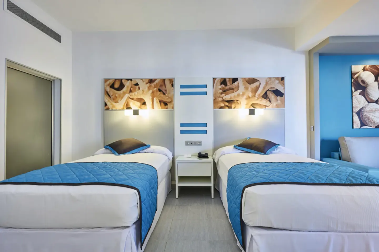 Family Suite twin beds with blue runners and bedside table at Hotel Riu Dunamar.
