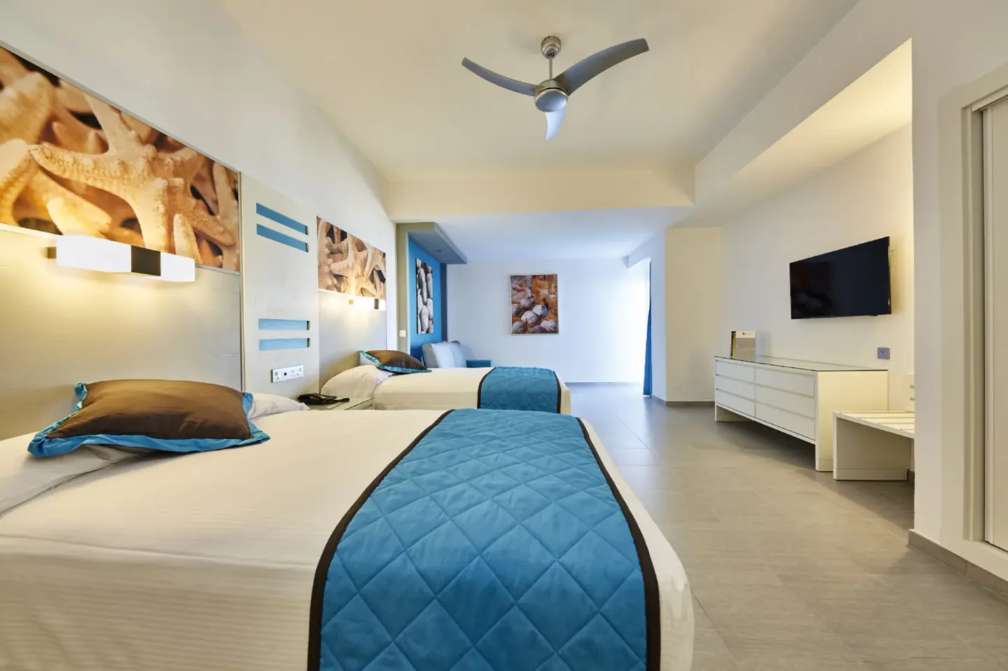 Family Suite two-bed room with blue bed runners and wall-mounted TV at Hotel Riu Dunamar.