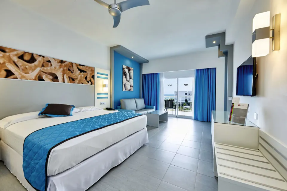 Ocean View room with king bed, balcony, and blue accents at Hotel Riu Dunamar.