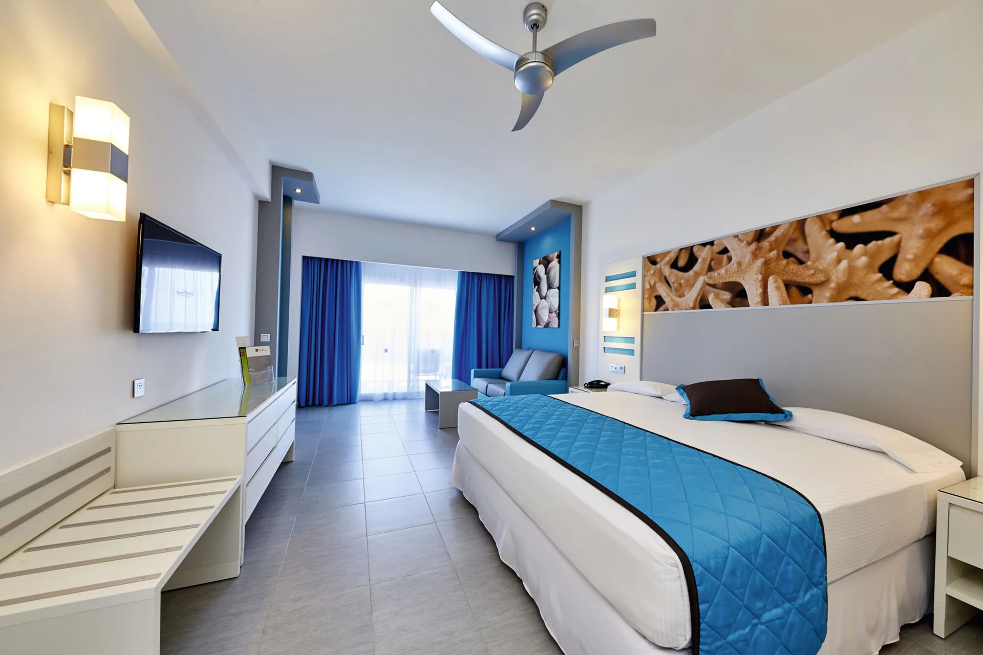 Oceanfront standard room with king bed, TV, sofa, and balcony doors at Hotel Riu Dunamar.