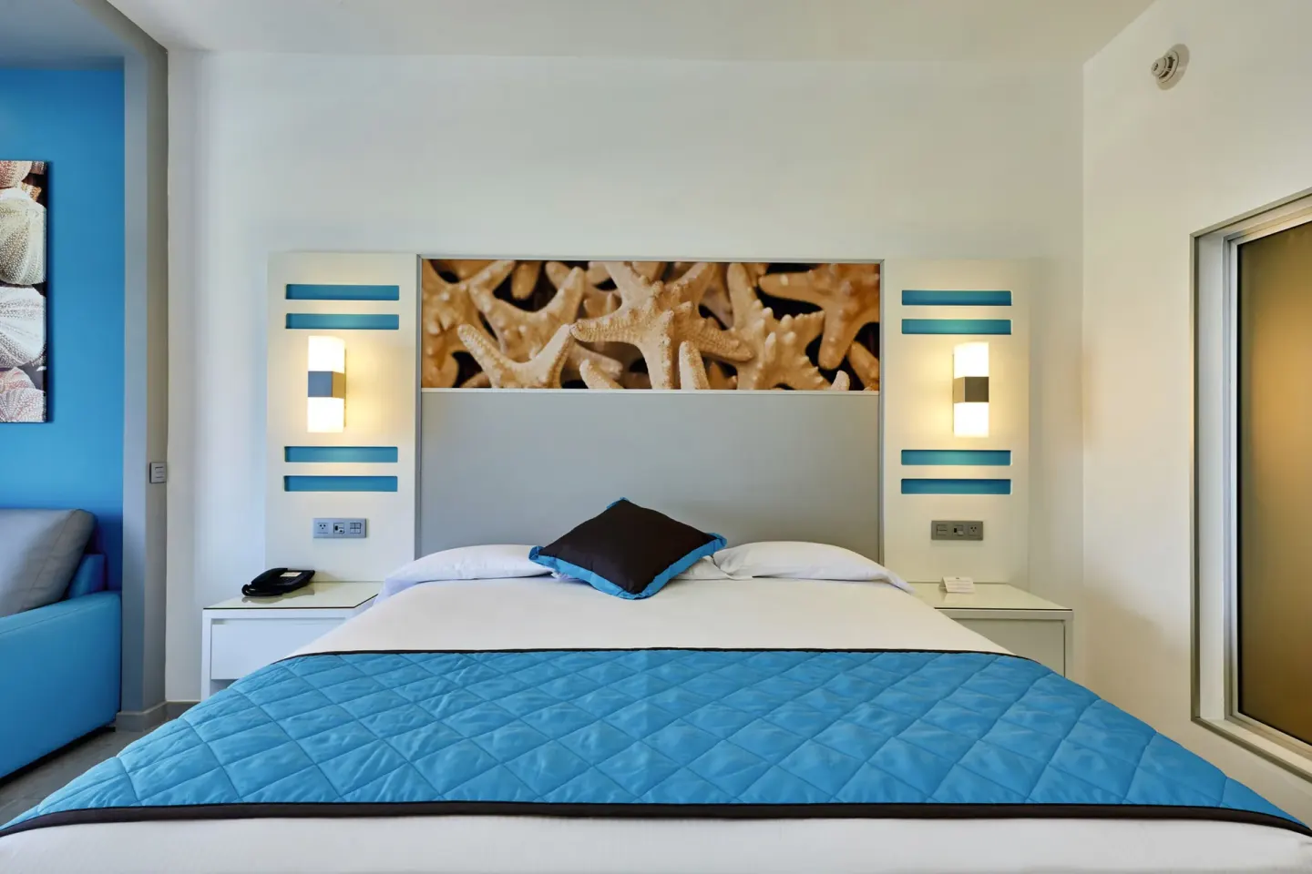King bed with blue runner and starfish headboard art in an oceanfront room at Hotel Riu Dunamar.