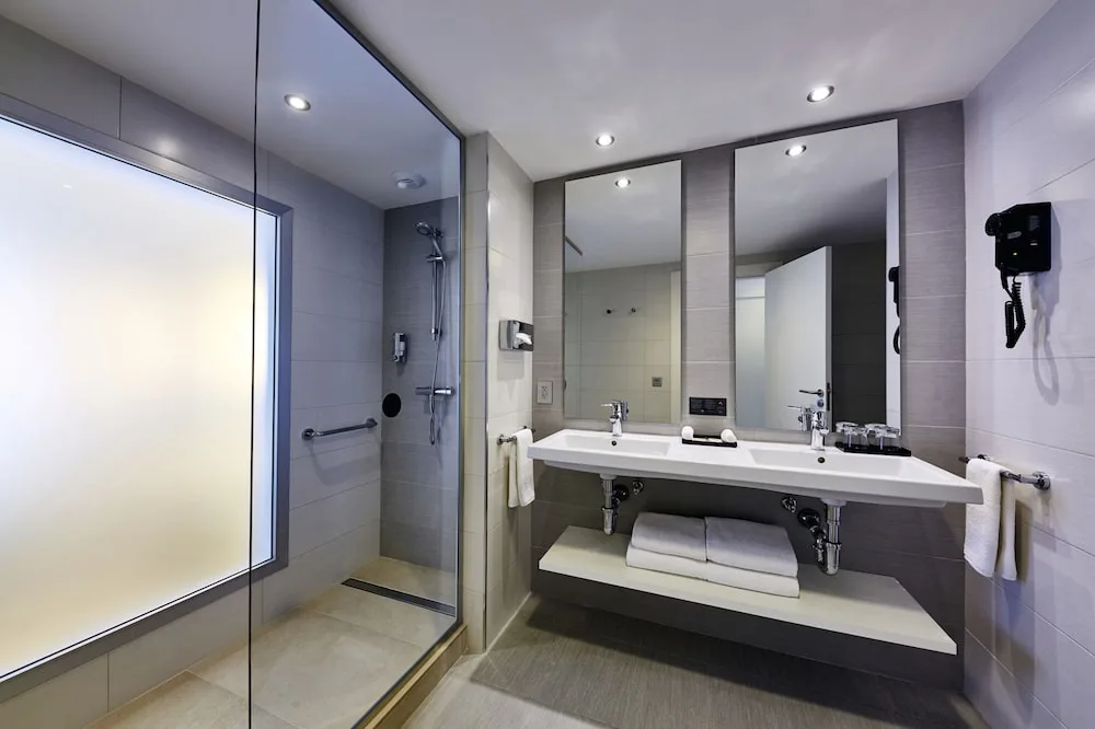Standard room bathroom with glass shower and double sink at Hotel Riu Dunamar.