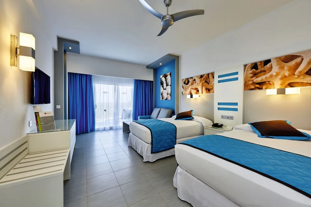 Standard room with two beds, balcony curtains and ceiling fan at Hotel Riu Dunamar.