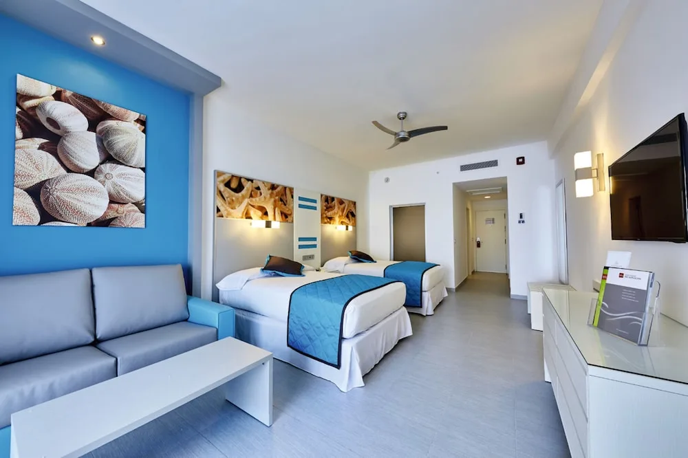 Standard room with two beds, sofa and TV at Hotel Riu Dunamar.